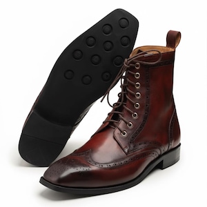 May include: A pair of brown leather boots with brogue detailing and a lace-up design. The boots have a square toe and a dark sole. One boot is upright, while the other is displayed with the sole facing up.