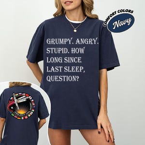 Op de afbeelding: Marineblauw T-shirt met de witte tekst "GRUMPY. ANGRY. STUPID. HOW LONG SINCE LAST SLEEP, QUESTION?". De achterkant van het shirt heeft een cirkelvormige afbeelding met de tekst "PROJECT HAIL MARY". Het shirt is gelabeld "COMFORT COLORS".