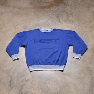 May include: A blue sweatshirt with the word "HEET" printed across the chest in a darker blue. The collar, cuffs, and hem feature white and blue striped detailing. The sweatshirt is made of a soft material.