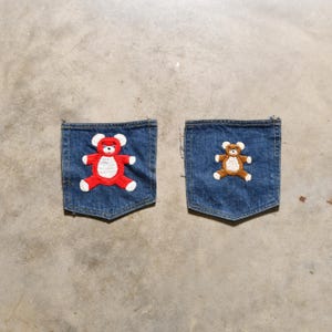 May include: Two denim pockets with embroidered teddy bears. The left pocket has a red teddy bear and the right pocket has a brown teddy bear.