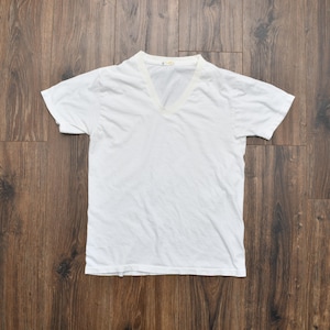May include: A plain white short-sleeved t-shirt featuring a V-neckline. The garment is constructed from a lightweight fabric and includes a small, rectangular interior neck label positioned at the center of the collar seam.