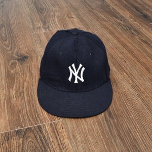 May include: A navy blue baseball cap with a white "NY" logo on the front. The cap has a curved brim and a rounded crown. The hat is made of a soft material and is likely a sports team accessory.