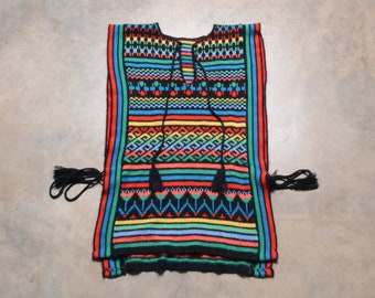 May include: A colorful knitted poncho with black tassels. The poncho has a geometric pattern in shades of red, blue, green, yellow, and black.