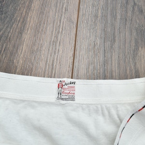 Puede incluir: Primer plano de un short Jockey blanco con una etiqueta. La etiqueta presenta un dibujo de un hombre con ropa roja y blanca. La etiqueta tambi&eacute;n tiene las palabras "Jockey Short" y "Cooper's".