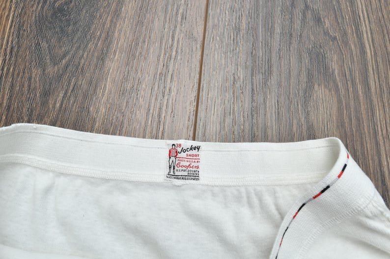 Puede incluir: Primer plano de un short Jockey blanco con una etiqueta. La etiqueta presenta un dibujo de un hombre con ropa roja y blanca. La etiqueta tambi&eacute;n tiene las palabras "Jockey Short" y "Cooper's".