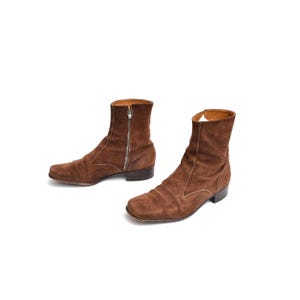 Puede incluir: Un par de botines de ante marrón. Los botines tienen punta cuadrada, cremallera lateral y tacón bajo. Los botines son de color marrón cálido y parecen ser vintage.