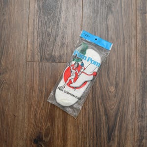 May include: A pair of white "Pom Pom" full cushion foot socks in a clear plastic package. The packaging features a red circle with a woman and a man, and the text "Pom Pom" in blue.