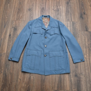May include: A light blue jacket with four front pockets and a notched collar. The jacket has three buttons down the front and buttons on the cuffs. The interior lining features a colorful geometric pattern. The jacket is made of a soft, textured fabric.