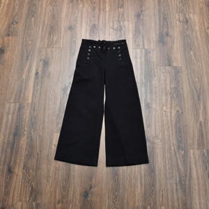May include: Black wide-leg pants with a high waist and multiple decorative buttons. The pants have a drawstring closure and a classic, timeless design. The fabric appears to be a medium-weight material, suitable for various seasons.