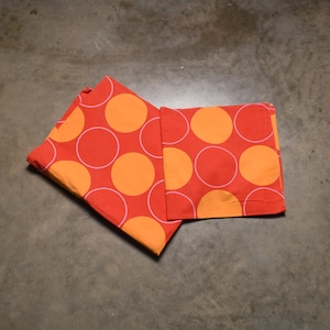 May include: Two red fabric placemats with a white outline and orange polka dots.