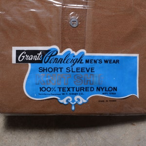May include: Two brown short-sleeved shirts in plastic packaging. The label reads "Grants Pennleigh Men's Wear Short Sleeve Knit Shirt 100% Textured Nylon Satisfaction Guaranteed W.T. Grant Co. WPL 12950 Made in Taiwan."
