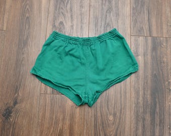 May include: Emerald green athletic shorts with an elastic waistband. The shorts are made of a soft, lightweight fabric. The shorts are a vintage style and are perfect for running or other athletic activities.