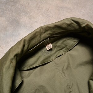K&ouml;nnte beinhalten: Nahaufnahme des inneren Kragens einer gr&uuml;nen Milit&auml;rjacke mit einem Gr&ouml;&szlig;enetikett mit der Aufschrift "Regular Medium".