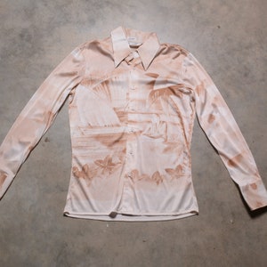 May include: A long-sleeved, button-up shirt with a light brown background and a brown print of palm trees and a beach scene.