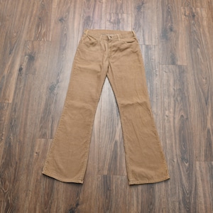 May include: A pair of tan corduroy pants featuring a classic five-pocket design, a button and zipper fly closure, and a straight-leg cut. The fabric has a distinct vertical ribbed texture throughout, with visible stitching along the seams.