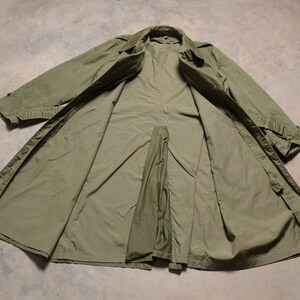 K&ouml;nnte beinhalten: Ein gr&uuml;ner Trenchcoat im Milit&auml;rstil mit Knopfleiste und G&uuml;rtel. Der Mantel liegt flach und offen und zeigt das Futter.