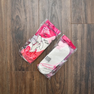 May include: Two packages of Pro Peds Pom Pom sport socks in clear plastic wrapping. The packaging features pink and white branding with text including Pro Peds, Pom Pom, and Sport Socks. The socks inside are white with pink accents.