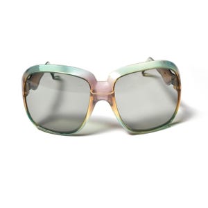 Puede incluir: Un par de gafas de sol cuadradas de color verde, rosa y marrón con lentes grises.