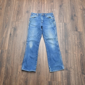 May include: Blue denim jeans with a classic five-pocket design. The jeans have a faded wash and a slight flare at the bottom. The jeans are laid flat on a wooden surface.