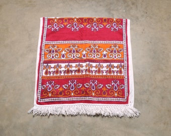 May include: A red, orange, and white patterned rug with a white fringe border. The rug has a traditional design with floral motifs.