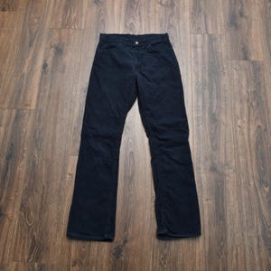 May include: Dark navy blue corduroy trousers. The trousers feature a classic five-pocket design with a button and zip closure. The corduroy fabric has vertical ridges. The trousers are laid flat on a wooden surface.