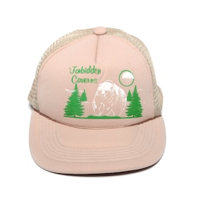 May include: A tan and brown mesh trucker hat with a white bear and green trees graphic. The text "Forbidden Caverns" is printed on the front of the hat.