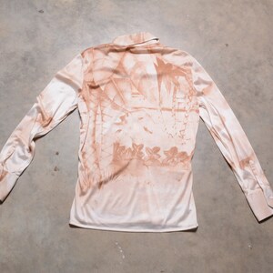 May include: A long-sleeved, light pink shirt with a brown floral print. The shirt has a collared neckline and button closure.