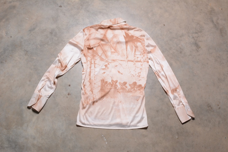 May include: A long-sleeved, light pink shirt with a brown floral print. The shirt has a collared neckline and button closure.