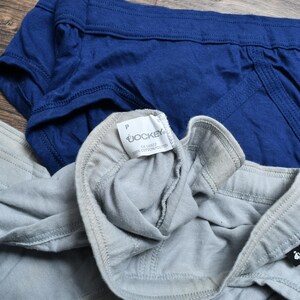 Puede incluir: Dos calzoncillos Jockey azules y grises, con el logo de Jockey visible. Los calzoncillos son de tela suave y est&aacute;n sobre una superficie de madera.