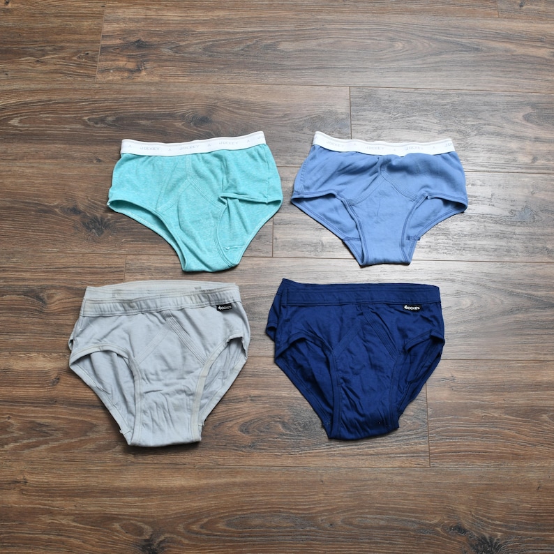 Puede incluir: Cuatro pares de calzoncillos en tonos azules y grises se muestran sobre una superficie de madera. Cada par tiene una cintura blanca. Los colores incluyen turquesa, azul claro, gris y azul marino. Los calzoncillos son de un material suave y c&oacute;modo.
