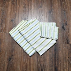 May include: A set of white bed sheets with blue and green stripes. The sheets are folded and arranged on a dark wood surface. The set includes a fitted sheet, a flat sheet, and pillowcases.