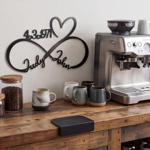 May include: A black metal wall sign featuring an infinity symbol intertwined with a heart shape. The sign includes the names Judy and John in cursive script and the date 4.3.1971 with small heart accents between the numbers.