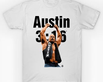 May include: White t-shirt featuring a graphic of a bald man with arms raised, wearing a black vest and a black towel. The text "Austin 3:16" is printed in large, bold, black letters above the man.