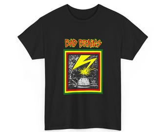 May include: A black short-sleeve t-shirt featuring a graphic print with the text BAD BRAINS in yellow and red. The design includes a yellow lightning bolt striking a white dome building, framed by a red, yellow, and green square border.