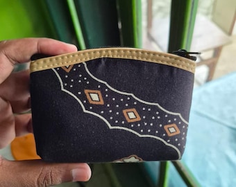 May include: A small, rectangular black coin purse with a decorative pattern of white dots and diamond shapes, accented with tan and gold trim. The purse has a zipper closure.