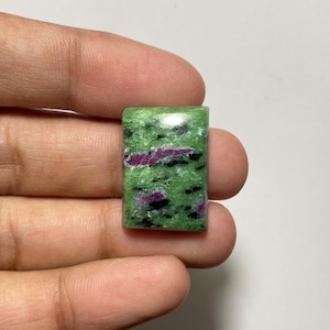 May include: A rectangular polished gemstone featuring a vibrant green base color with distinct, irregular magenta-pink inclusions and scattered black mineral spots throughout the surface, showcasing a smooth, reflective, and flat-faced finish.