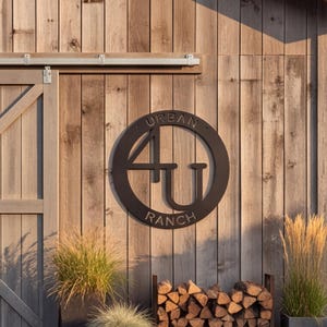 May include: A circular black metal wall sign featuring the text "URBAN" at the top and "RANCH" at the bottom, with the large characters "4U" centered within the frame. The sign is mounted on a vertical wooden plank wall surface.
