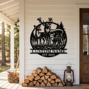 Könnte beinhalten: Schwarzes Metallschild mit einer Hirschfamilie in kreisförmigem Design. Das Schild zeigt einen Hirsch, eine Hirschkuh und ein Jungtier mit dem Text "CUSTOM NAME EST 2025". Es ist an einer weißen Wand angebracht.