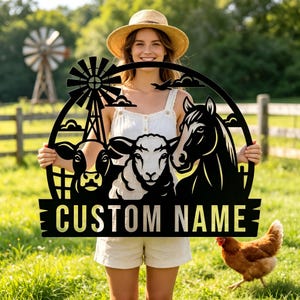 Pode incluir: Placa de fazenda de metal preto com uma vaca, uma ovelha e um cavalo, com um moinho de vento e nuvens. A placa tem o texto "CUSTOM NAME" em uma faixa. A placa é segurada por uma pessoa em um campo.