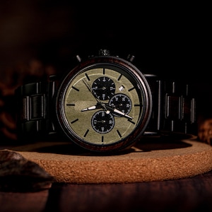 May include: A wooden chronograph watch with a dark brown wooden band and a green face. The watch has three sub-dials and a date window. The watch is displayed on a round, brown surface.