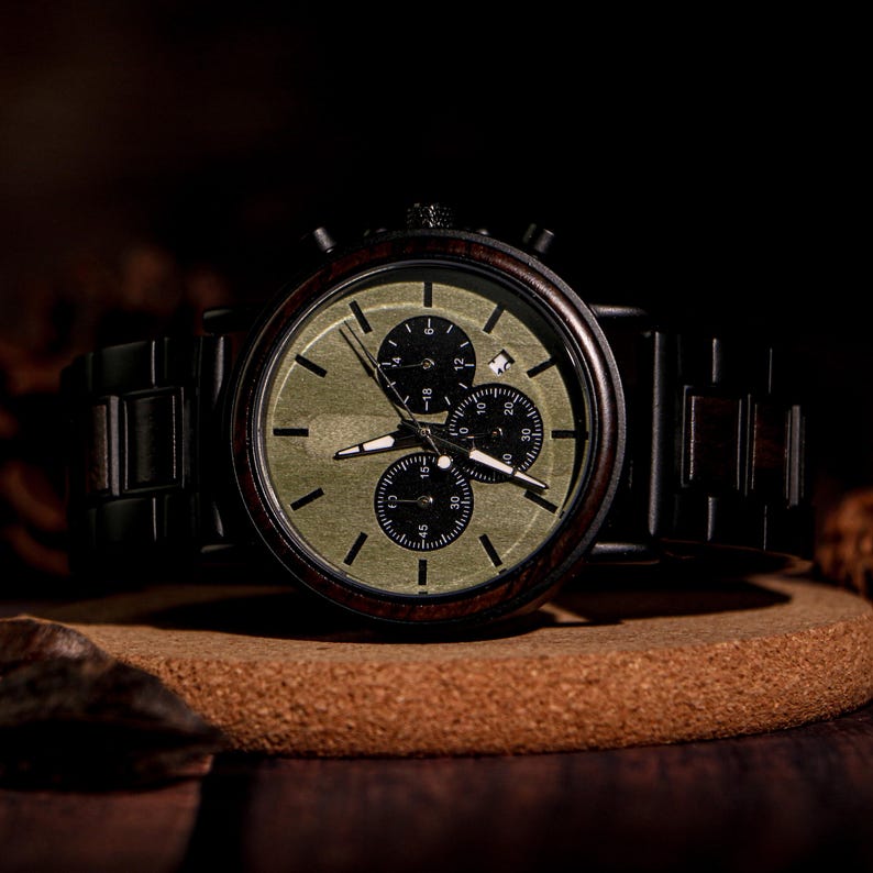 May include: A wooden chronograph watch with a dark brown wooden band and a green face. The watch has three sub-dials and a date window. The watch is displayed on a round, brown surface.