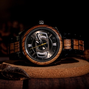 May include: A wooden wristwatch with a dark face and a brown wooden bezel. The watch has a black band with wooden links. The watch face has a unique design with visible gears and the word "Voodoo" at the bottom.