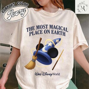 A person wearing a white t-shirt with a graphic design featuring a wizard's hat and broom, along with the text "The most magical place on earth" and the Walt Disney World logo.