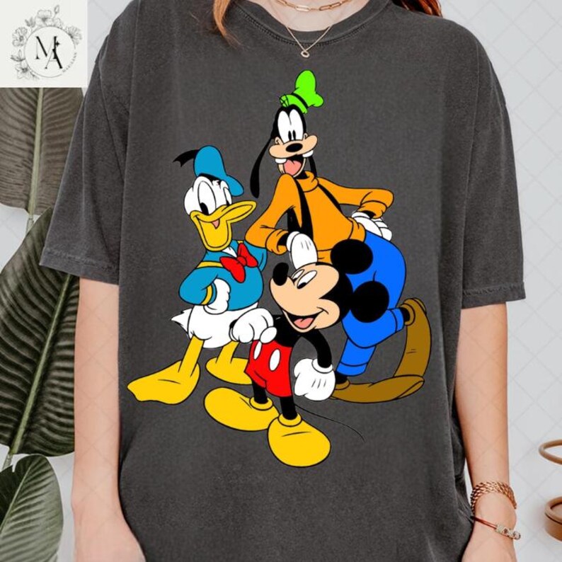 A person wearing a gray t-shirt with a graphic design featuring the Disney characters Goofy, Mickey Mouse, and Donald Duck.