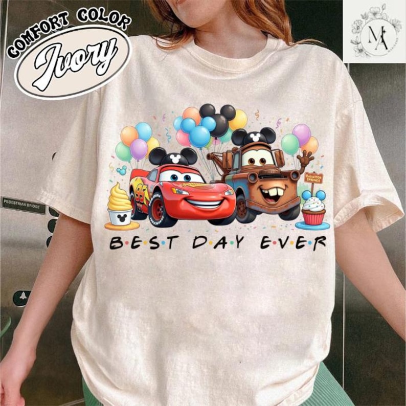 A person wearing a white t-shirt with a graphic design featuring characters from the Disney movie Cars, including Lightning McQueen, Lightning McQueen's car, and a cake.