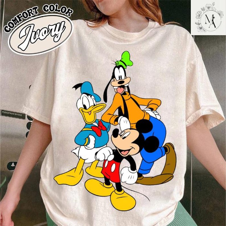A person wearing a white t-shirt with a colorful graphic of Disney characters, including Mickey Mouse, Donald Duck, and Goofy.