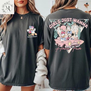 a woman wearing a black t-shirt with a graphic design on the back. The design includes Minnie Mouse and Donald Duck riding in a spaceship, along with the text "Girls Just Wanna Have Fun".