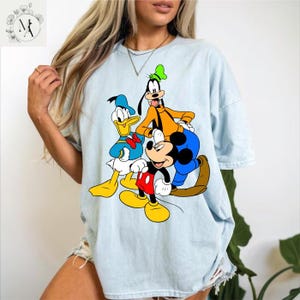 A woman wearing a light blue t-shirt with a graphic of Disney characters Mickey Mouse, Donald Duck, and Goofy.