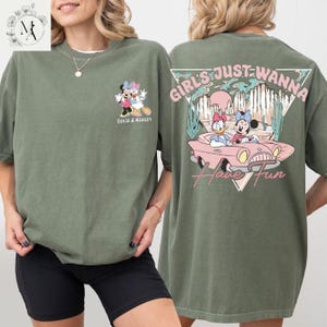 A woman wearing a green t-shirt with a graphic design featuring Minnie Mouse and Donald Duck, along with the text "Girls Just Wanna Have Fun".