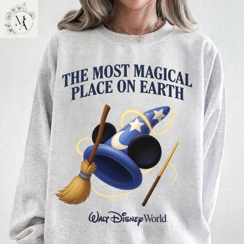 A person wearing a gray sweatshirt with a graphic design featuring a wizard's hat, broom, and wand, along with the text "The most magical place on earth" and the Walt Disney World logo.
